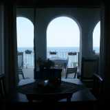 Dalla sala da pranzo intravediamo una veranda delineata da archi in cemento bianco, attraverso cui scorgiamo quel mare che sembra ricreare il paesaggio di uno dei tanti ritratti appesi al muro